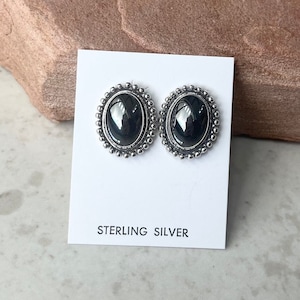 May include: A pair of sterling silver earrings with black oval stones set in a beaded bezel.