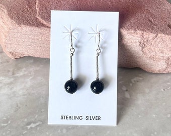 May include: A pair of sterling silver dangle earrings with black onyx beads. The earrings are on a white card with the text "Sterling Silver".