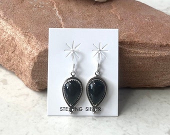 May include: A pair of sterling silver earrings with black gemstone teardrop dangles. The earrings are displayed on a white card with the text "Sterling Silver".