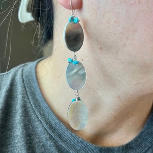 May include: Dangling earrings with three oval, iridescent mother-of-pearl pendants. Each pendant is connected by silver-toned wire and accented with small turquoise beads. The earrings have a silver-toned hook.