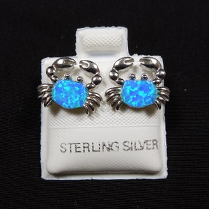 May include: A pair of sterling silver earrings featuring a blue opal crab design. The earrings are displayed on a white card with the words "Sterling Silver" printed on it.