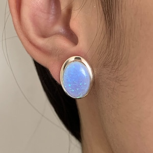 Puede incluir: Un par de pendientes de botón de plata con piedras de ópalo azul de forma ovalada.