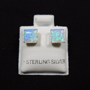 May include: A pair of sterling silver square stud earrings with iridescent opal stones. The earrings are displayed on a white card with the words "Sterling Silver" printed on it.
