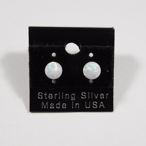 Könnte beinhalten: Ein Paar weiße Opal-Ohrstecker auf einer schwarzen Karte mit dem Text "Sterling Silver Made in USA".