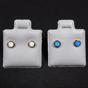 Peut inclure: Deux paires de boucles d'oreilles clous sur des cartes d'exposition. Une paire est en opale blanche et l'autre en opale bleue.
