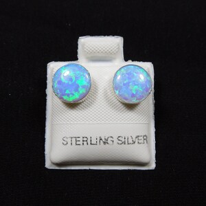 Könnte beinhalten: Ein Paar Ohrstecker aus Sterlingsilber mit blauen Opal-Steinen. Die Ohrringe werden auf einer weißen Karte mit dem Aufdruck "Sterling Silver" präsentiert.