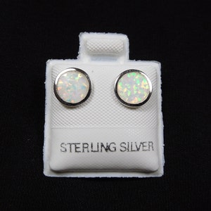 Peut inclure: Une paire de boucles d'oreilles en argent sterling avec des pierres d'opale blanches. Les boucles d'oreilles sont présentées sur une carte blanche avec les mots "Sterling Silver" imprimés dessus.