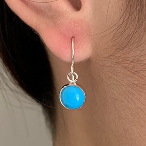 May include: A pair of silver earrings with a turquoise stone. The earrings are small and delicate, and the turquoise stone is a bright blue colour.