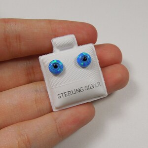 Puede incluir: Un par de pendientes de botón de ópalo azul en una tarjeta blanca con el texto "Sterling Silver".