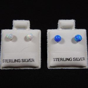 Puede incluir: Dos pares de pendientes de botón de plata de ley con piedras de ópalo. Un par tiene piedras de ópalo blancas y el otro par tiene piedras de ópalo azules.