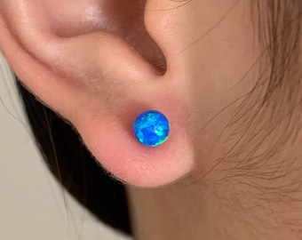 Könnte beinhalten: Nahaufnahme eines Ohres mit einem blauen Opal-Ohrstecker. Der Ohrstecker ist eine runde, flache Scheibe mit einem blauen und grünen, schillernden Finish.