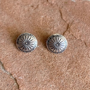 May include: A pair of silver earrings with a circular design featuring a sunburst pattern.