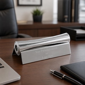 Op de afbeelding: Een zilverkleurige metalen bureau-naamplaatjeshouder met een cilindrisch bovengedeelte en een plat, schuin voorpaneel. Het voorpaneel is voorzien van de gegraveerde tekst 'Your Personalization or Logo Here' in een schreefloos lettertype.