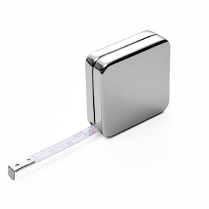 May include: A silver metal tape measure with a white tape extending from the side. The tape measure is about 2 inches wide and 2 inches tall.