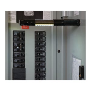 Puede incluir: Una lámpara de trabajo LED negra y plateada está colocada dentro de un panel eléctrico. La luz ilumina el interior del panel, que incluye disyuntores y etiquetas. El panel es gris y la lámpara tiene una tira de LED blanca brillante.