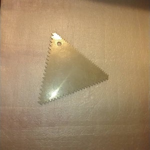 May include: A silver triangle-shaped cake decorating tool with a serrated edge and a small hole in the center.