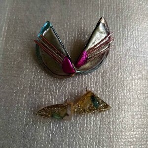 May include: A pair of earrings with a gold and silver finish. The larger earring is a geometric shape with a pink accent. The smaller earring is a triangular shape with gold glitter and a blue accent.