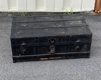 May include: A black wooden vintage trunk with metal hardware and a latch. The trunk has a worn and distressed look.