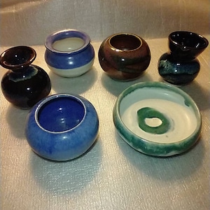May include: Six small ceramic pots in various colors and designs. The pots are all different shapes and sizes, and some have a white glaze.