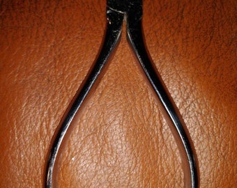 May include: Silver-toned metal nail clippers with a pointed tip. The clippers have a small inscription that reads "Stahl" and "Germany".