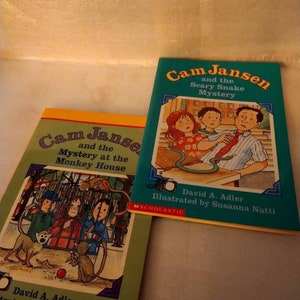 May include: Two paperback children's books with green and yellow covers. The books are titled "Cam Jansen and the Mystery at the Monkey House" and "Cam Jansen and the Scary Snake Mystery". Both books feature illustrations of children and a monkey on the covers.