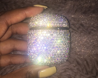May include: A white Airpod case covered in clear iridescent rhinestones.