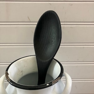 May include: A black wooden spoon in a white enamel jug with a black rim.