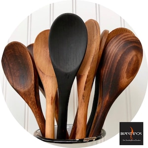 May include: A close-up of a set of wooden spoons, some are stained a dark brown colour, and one is painted black. The spoons are in a white enamelware container with a black rim. The text "BURNT ENDS" is visible in the lower right corner of the image.