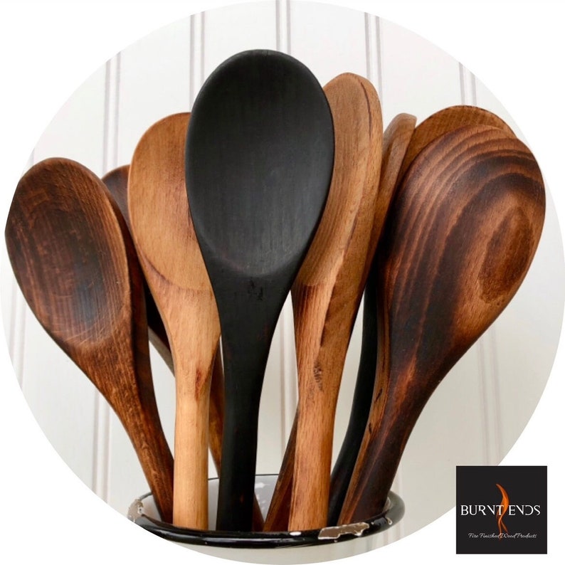 May include: A close-up of a set of wooden spoons, some are stained a dark brown colour, and one is painted black. The spoons are in a white enamelware container with a black rim. The text "BURNT ENDS" is visible in the lower right corner of the image.