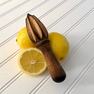 May include: A wooden lemon reamer with a dark brown finish and a textured surface. The reamer is sitting on a white surface with two lemons.