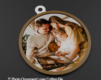 Könnte beinhalten: Runder Foto-Ornament mit einem Familienfoto im Inneren. Das Ornament hat einen goldfarbenen Rand und eine weiße Schlaufe zum Aufhängen. Das Bild zeigt eine dreiköpfige Familie, die sich ein Fotoalbum ansieht. Text unten: "3" Photo Ornament Laser Cutting File + Canva Frames Photo Template."