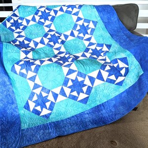 May include: A blue and white quilt with a star pattern. The quilt features a repeating design of white triangles and blue circles, with a border of solid blue. The quilt is draped over a chair.