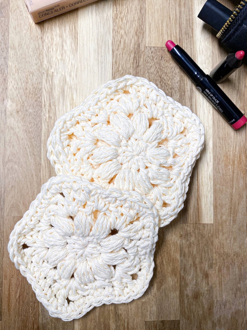 Pode incluir: Duas toalhas de croch&ecirc; quadradas creme com um design floral. As toalhas s&atilde;o feitas de um fio macio e texturizado. O fundo inclui itens de maquiagem em uma superf&iacute;cie de madeira.
