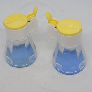 May include: Two small blue and white salt and pepper shakers with yellow lids. The shakers have a ribbed design.