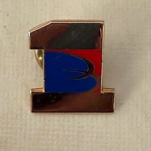May include: A gold-toned metal pin in the shape of the number one. The pin features a design with a black top section, a red section, and a blue section with a curved shape. The pin has a gold-colored pin back.