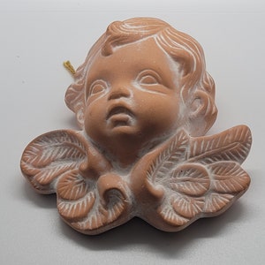 May include: A terracotta cherub figurine with wings made of leaves. The cherub has a sweet expression and is painted in a light brown color.