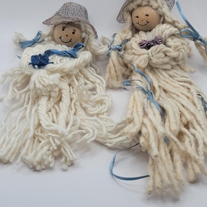 May include: Two handmade yarn dolls with wooden heads and painted faces. They are wearing gray hats and have long white yarn hair with blue ribbon accents.