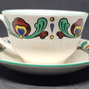 May include: A white teacup and saucer with a green rim and a floral design in red, orange, yellow, blue, and green.