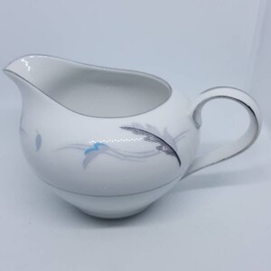 May include: White ceramic creamer with a silver rim and a delicate floral design in shades of blue, pink, and gray.