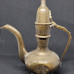 May include: A brass teapot with an ornate design and a hinged lid. The teapot has a curved spout and a handle.