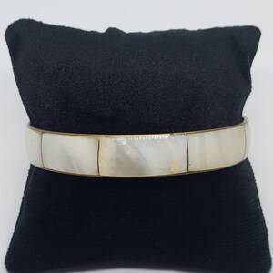May include: A white and gold bangle bracelet with a decorative design of inlaid mother of pearl squares.