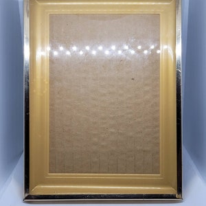 May include: A gold picture frame with a light brown mat. The frame has a simple, classic design.