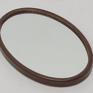 May include: A brown oval-shaped framed mirror with a reflective surface.