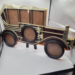 May include: A vintage-style car shaped picture frame with three photo openings. The frame is made of brown plastic with gold accents. The frame is designed to look like a classic car with a rounded hood, a windshield, and a spare tire on the back.