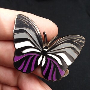 May include: A black, white, and purple butterfly pin with a silver finish. The butterfly has a striped pattern on its wings.
