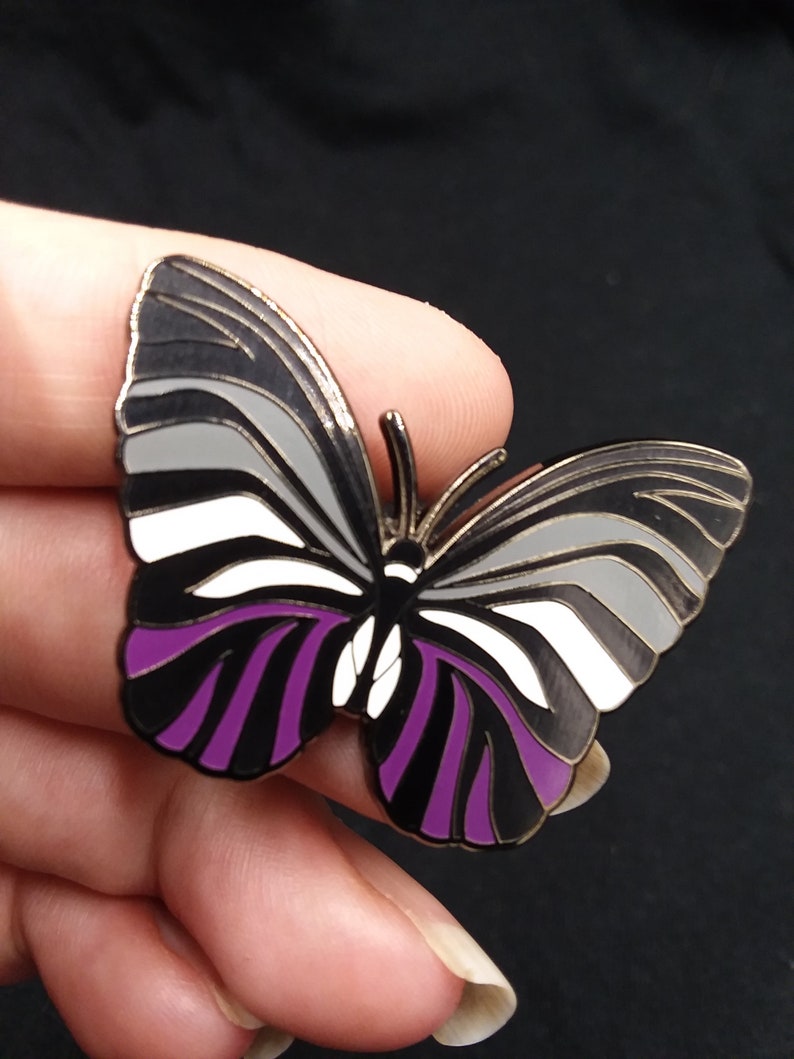 May include: A black, white, and purple butterfly pin with a silver finish. The butterfly has a striped pattern on its wings.