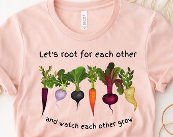May include: A pink t-shirt with a graphic of colorful vegetables and the text "Let's root for each other and watch each other grow."