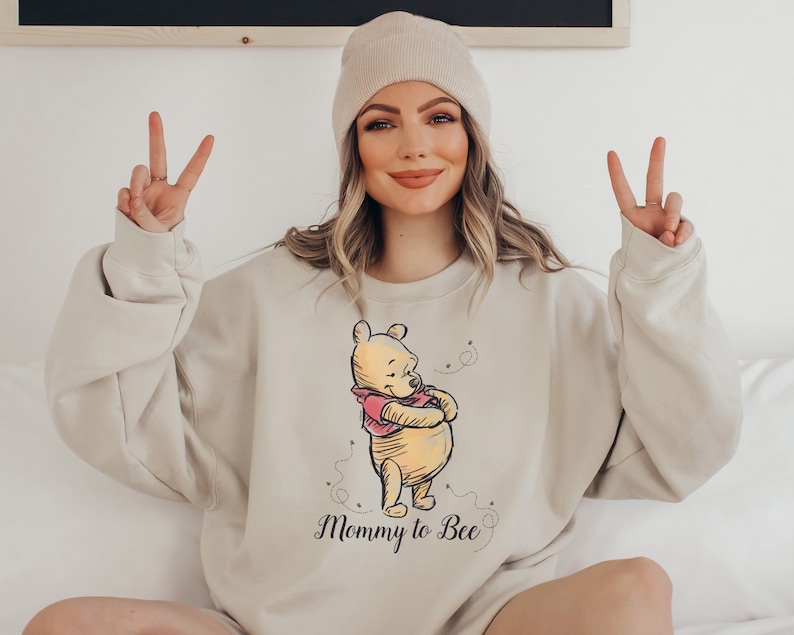 May include: A beige sweatshirt with a Winnie the Pooh illustration and the text "Mommy to Bee".