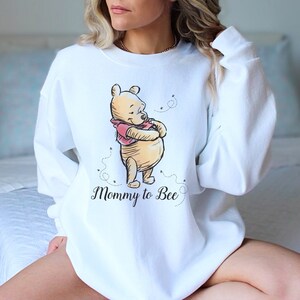 May include: White sweatshirt with a Winnie the Pooh illustration and the text "Mommy to Bee".