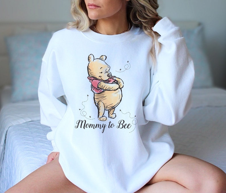 May include: White sweatshirt with a Winnie the Pooh illustration and the text "Mommy to Bee".
